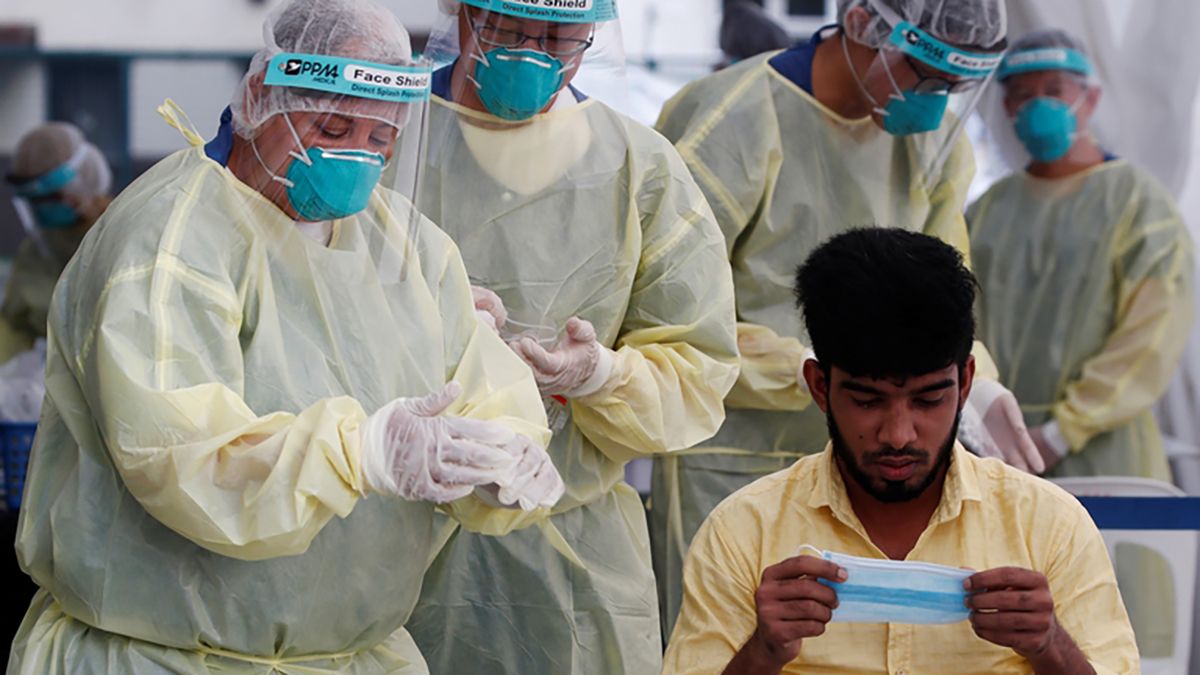 Médicos preparándose para realizarle una prueba de coronavirus a un trabajador migratorio en Singapur.