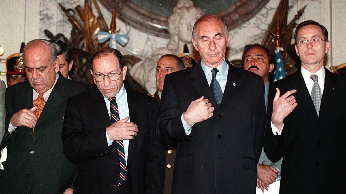 El entonces presidente de la Argentina, Fernando De la Rúa, se persigna, junto al encargado de negocios de la embajada de los Estados Unidos, Tomas Ducker, en un acto recordando el atentado a las Torres Gemelas en diciembre de 2001.
