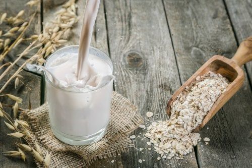 Granos de avena en una cuchara de madera y un vaso con bebida de avena