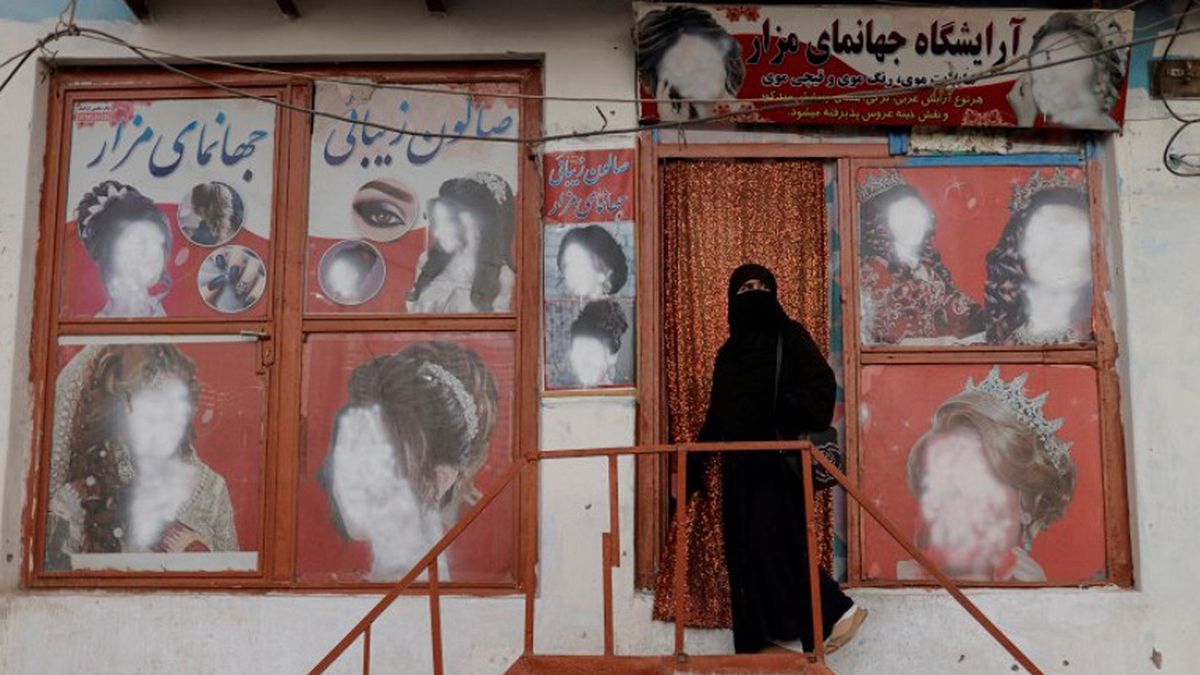 Una mujer con niqab entra en un salón de belleza donde los anuncios de mujeres han sido desfigurados por un comerciante en Kabul