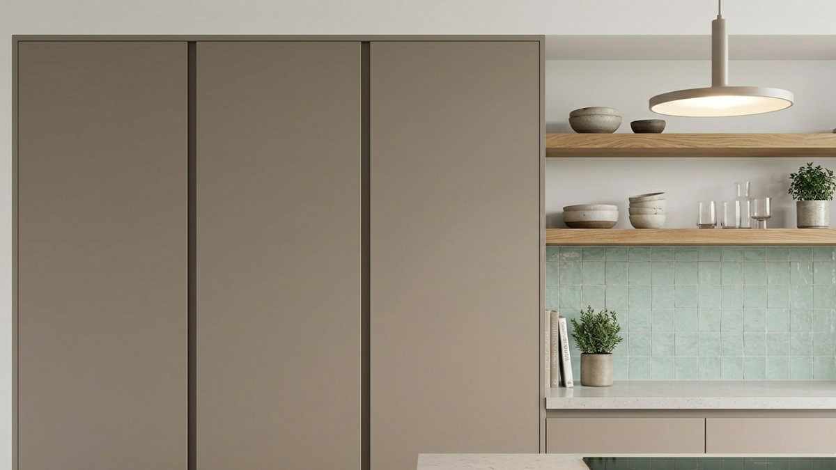 Esta imagen ilustra la dualidad de la tendencia. A la izquierda, muebles de piso a techo, lisos y sin manijas, color gris visón. A la derecha, una zona de mesada donde la alacena fue reemplazada por dos estantes flotantes de madera maciza, exhibiendo vajilla de cerámica artesanal.