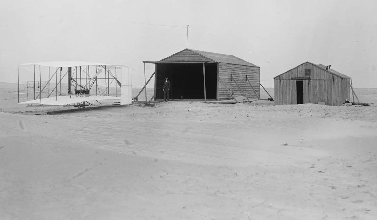 Esta foto es del 24 de noviembre de 1903, donde el Flyer está fuera del hangar (término que en esa época no existía) y, la construcción más chica, es la que se utilizaba como taller y alojamiento de los hermanos Wright en Kill Devil Hills, Kitty Hawk. Esta foto es del 24 de noviembre de 1903, donde el Flyer está fuera del hangar (término que en esa época no existía) y, la construcción más chica, es la que se utilizaba como taller y alojamiento de los hermanos Wright en Kill Devil Hills, Kitty Hawk.