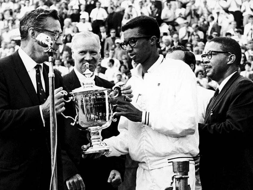 El 8 de septiembre de 1968 y, con 25 años, Ashe fue el primer jugador negro que se alzó con el título en el US Open, en el mismo court central ¡que hoy lleva su nombre! y al que algunas veces le habían prohibido la entrada: derrotó en la final al holandés Tom Okker por 14-12, 5-7, 6-3, 3-6 y 6-3. En la foto, detrás de él (y de anteojos), está su padre, Arthur, Sr.