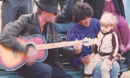 Luca Prodan con su guitarra acústica cantándole a un niño en el banco de una plaza Luca Prodan con su guitarra acústica cantándole a un niño en el banco de una plaza