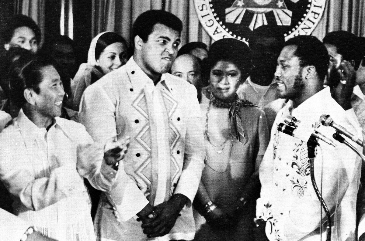 El 18 de septiembre de 1975, 12 días antes de la pelea, el dictador Ferdinando Marcos (izquierda) recibió a Muhammad Ali y a Joe Frazier en el palacio presidencial de Malacañang, en Manila, acompañado por su esposa, Imelda (en el centro). En dicho encuentro, cada boxeador apostó un millón de dólares a que ganaría el combate. El 18 de septiembre de 1975, 12 días antes de la pelea, el dictador Ferdinando Marcos (izquierda) recibió a Muhammad Ali y a Joe Frazier en el palacio presidencial de Malacañang, en Manila, acompañado por su esposa, Imelda (en el centro). En dicho encuentro, cada boxeador apostó un millón de dólares a que ganaría el combate.
