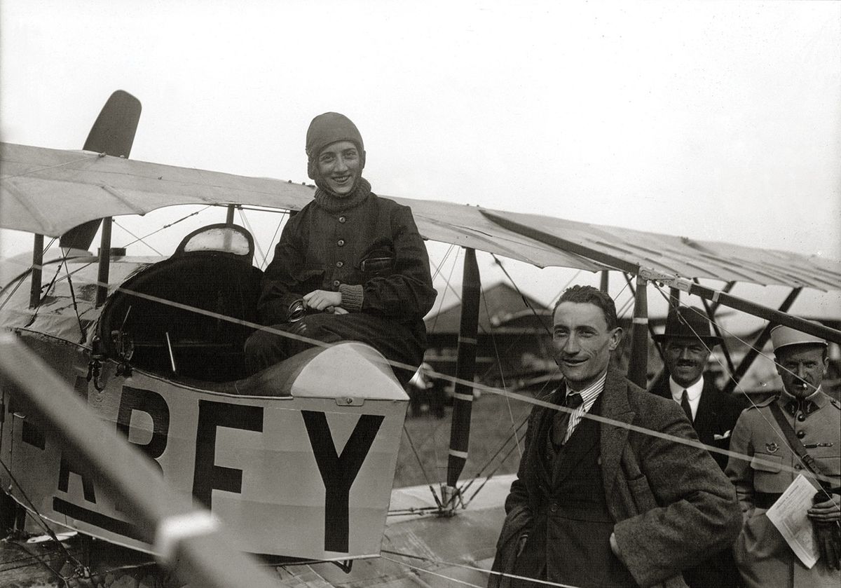 En el cockpit de su Caudron C.3 matrícula F-ABFY, posa con el aviador Auguste Maïcon en el Meeting del Aéroparc de Buc, un aeródromo que estaba ubicado 18 kilómetros al suroeste de París, que se realizó del 8 al 10 de octubre de 1920, y donde Adrianne realizó varias exhibiciones. El 23 de diciembre siguiente, llegaría por primera vez a nuestro país.
