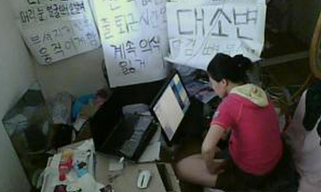 Chip Chan en su habitación, rodeada de carteles de protesta escritos a mano, mientras revisa su ordenador. Chip Chan en su habitación, rodeada de carteles de protesta escritos a mano, mientras revisa su ordenador.
