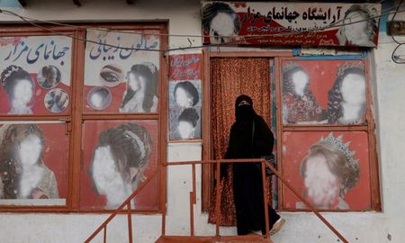 Una mujer con niqab entra en un salón de belleza donde los anuncios de mujeres han sido desfigurados por un comerciante en Kabul, Afganistán. Una mujer con niqab entra en un salón de belleza donde los anuncios de mujeres han sido desfigurados por un comerciante en Kabul, Afganistán.