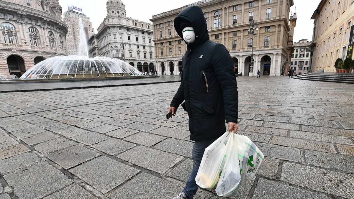 Un ciudadano genovés realiza sus compras cubriendo su cara con un barbijo por la pandemia.