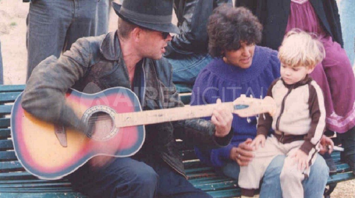 Luca Prodan con su guitarra acústica cantándole a un niño en el banco de una plaza