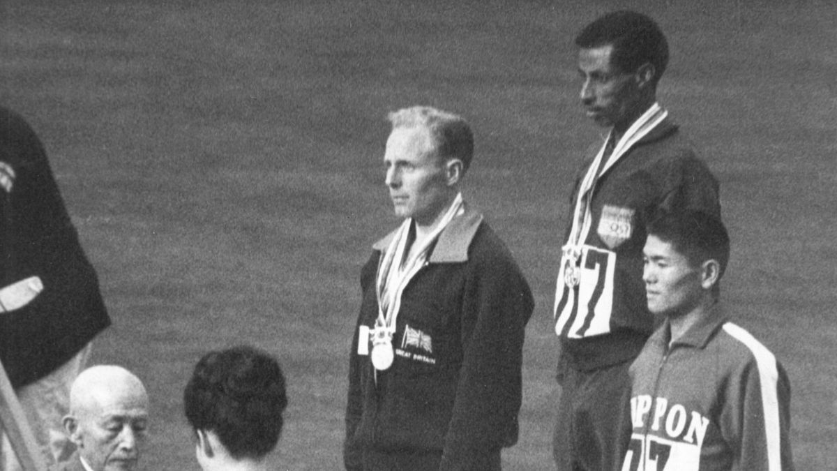 El podio del maratón de los Juegos Olímpicos de Tokio 1964, donde Bikila fue escoltado por el británico Basil Heatley (plata, a su derecha) y el japonés Kokichi Tsuburaya (bronce). El podio del maratón de los Juegos Olímpicos de Tokio 1964, donde Bikila fue escoltado por el británico Basil Heatley (plata, a su derecha) y el japonés Kokichi Tsuburaya (bronce).