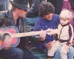Luca Prodan con su guitarra acústica cantándole a un niño en el banco de una plaza Luca Prodan con su guitarra acústica cantándole a un niño en el banco de una plaza
