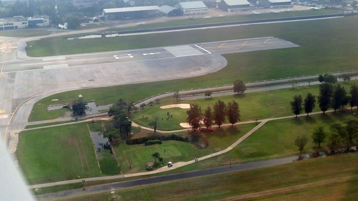 Un avión comercial sobrevuela la zona de dos bunkers del campo de golf (visto desde el oeste), a la altura de la cabecera 03R (Right, o derecha), la más larga de Don Mueang. La imagen muestra la cercanía entre los greens y el sector desde donde despegan o aterrizan las aeronaves. Un avión comercial sobrevuela la zona de dos bunkers del campo de golf (visto desde el oeste), a la altura de la cabecera 03R (Right, o derecha), la más larga de Don Mueang. La imagen muestra la cercanía entre los greens y el sector desde donde despegan o aterrizan las aeronaves.