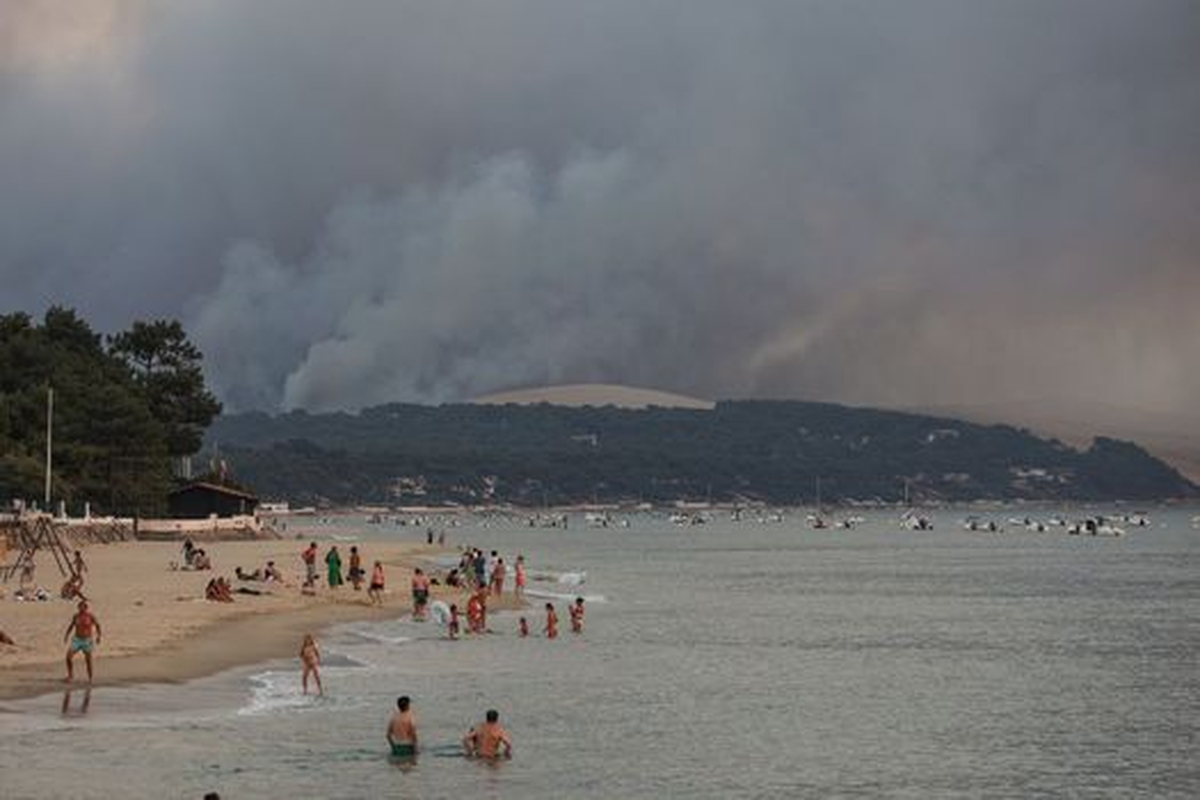 Personas nadando en la playa de Moulleau mientras el humo se eleva del incendio forestal en La Teste-de-Buch, en Francia.Foto: AFP - Agencia AFP