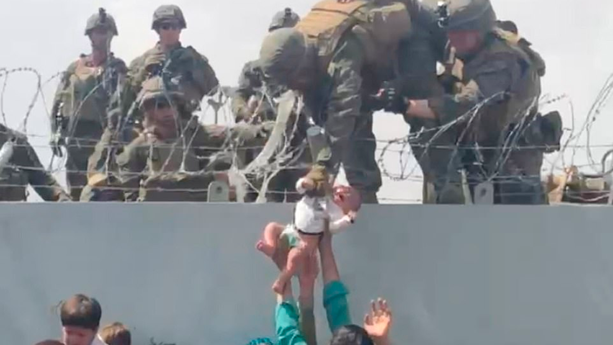 En la imagen se ve a un&nbsp;adulto entregando un bebe a un soldado estadounidense por encima de un alambre de púas en el aeropuerto de Kabul