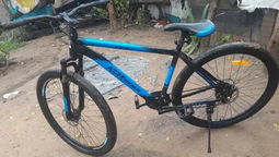 Bicicleta tipo balón, rodado 29, negra con detalles azules y una marca visible en el manubrio producto de un golpe.