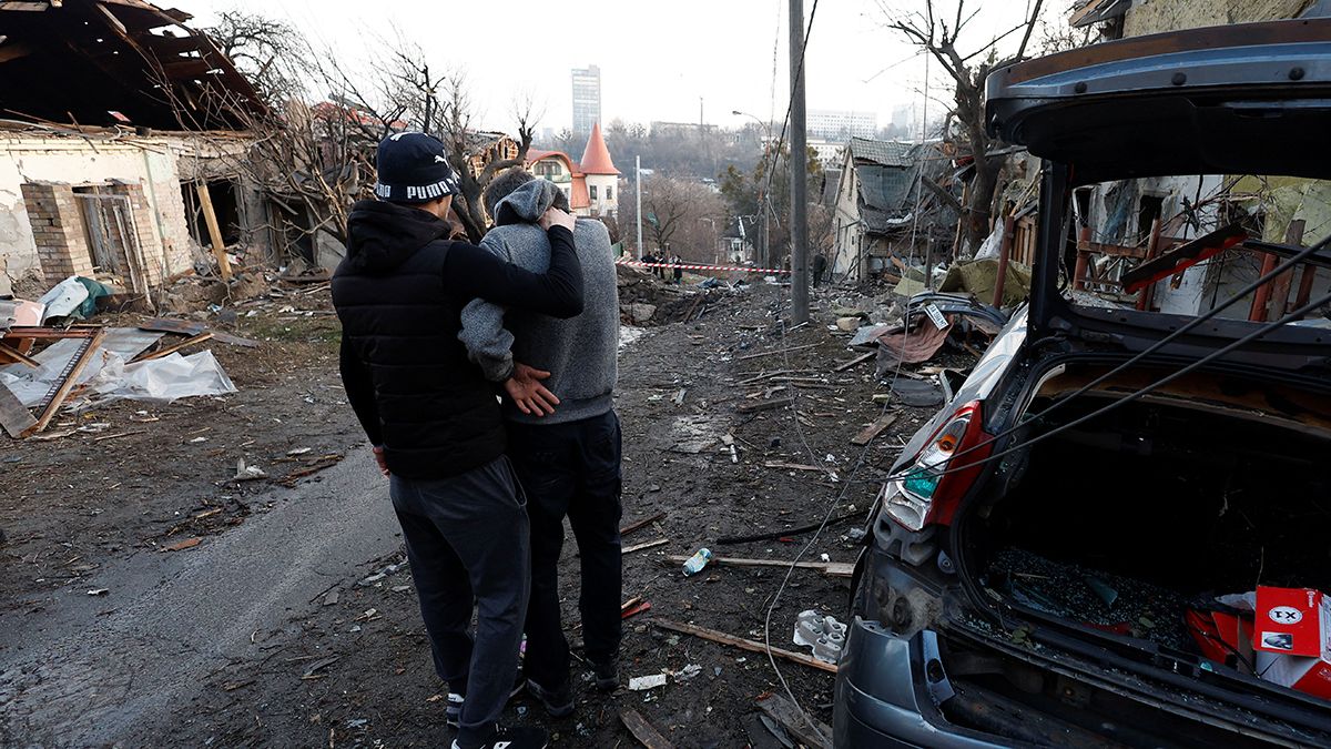 Un residente local abraza a su amigo mientras se paran junto a la casa y el automóvil dañados durante un ataque con misiles rusos, en medio del ataque de Rusia a Ucrania, en Kiev, Ucrania, el 31 de diciembre de 2022.