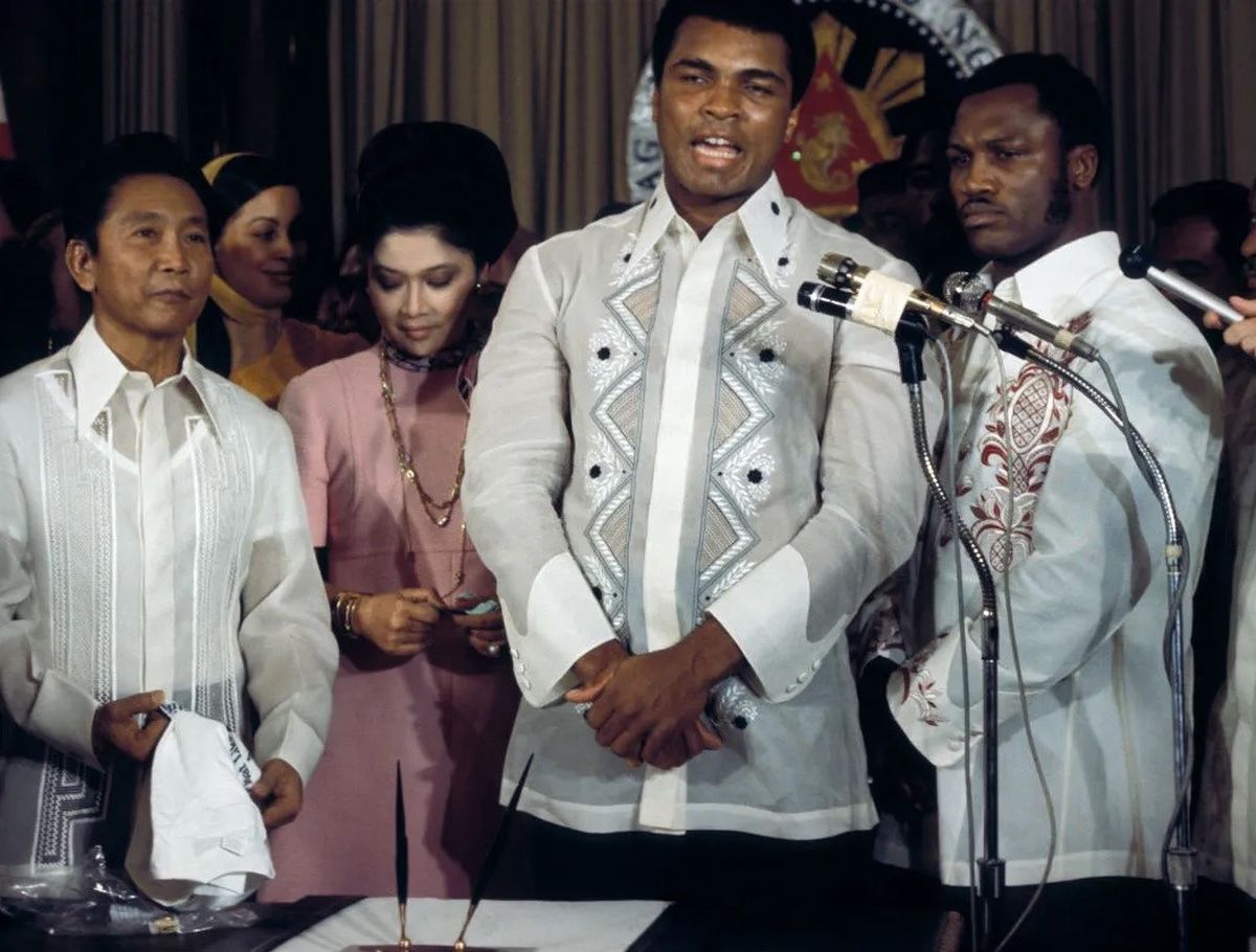 El 18 de septiembre de 1975, 12 días antes de la pelea, el dictador Ferdinando Marcos (izquierda) recibió a Muhammad Ali y a Joe Frazier en el palacio presidencial de Malacañang, en Manila, acompañado por su esposa, Imelda (en el centro). En dicho encuentro, cada boxeador apostó un millón de dólares a que ganaría el combate. El 18 de septiembre de 1975, 12 días antes de la pelea, el dictador Ferdinando Marcos (izquierda) recibió a Muhammad Ali y a Joe Frazier en el palacio presidencial de Malacañang, en Manila, acompañado por su esposa, Imelda (en el centro). En dicho encuentro, cada boxeador apostó un millón de dólares a que ganaría el combate.